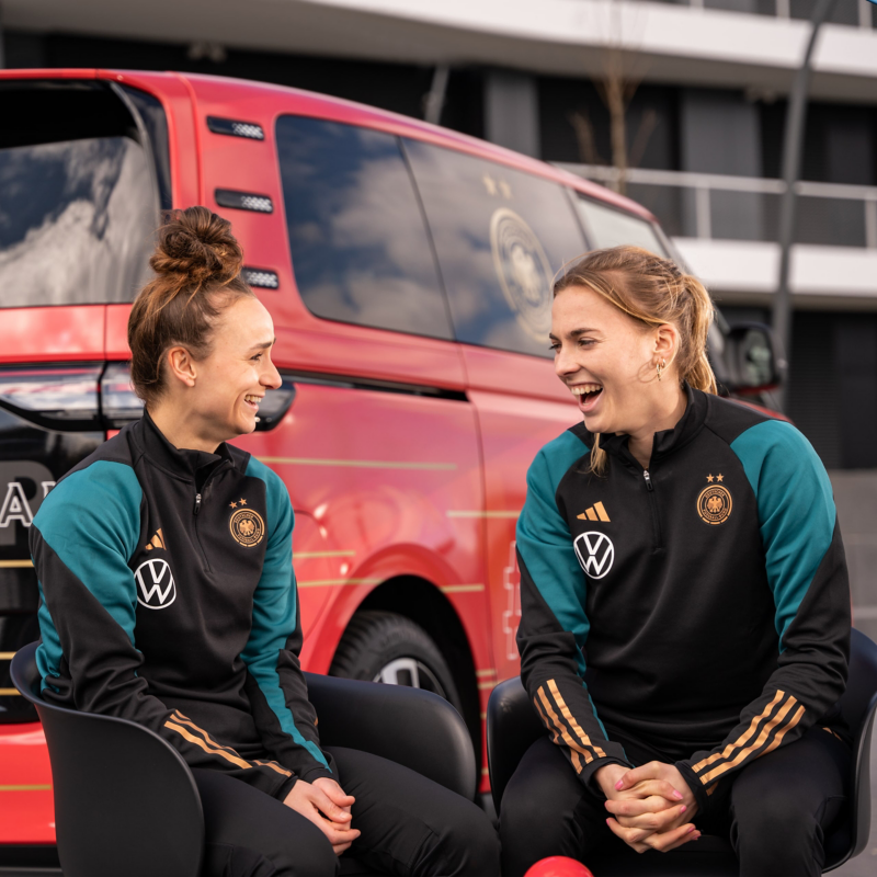 Zwei Frauen der DFB Frauen lachend vor dem VW ID. Buzz sitzend.