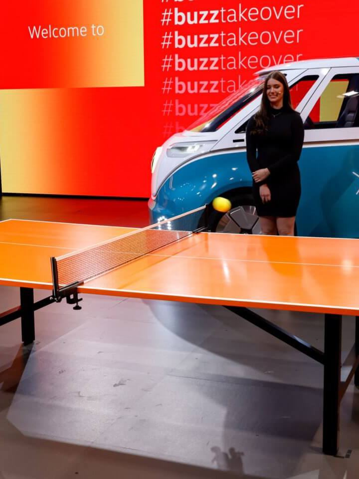 Zwei Männer spielen an einer Tischtennisplatte, der VW ID. Buzz steht im Hintergrund.