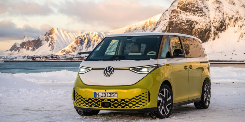 Der VW ID. Buzz steht in einer verschneiten Landschaft vor einem See, dahinter befindet sich ein Gebirge.