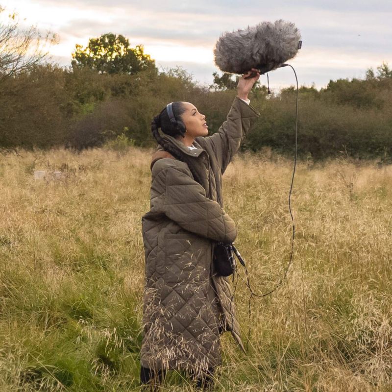 Jayda G hält ein Mikrofon in einer Naturlandschaft hoch.