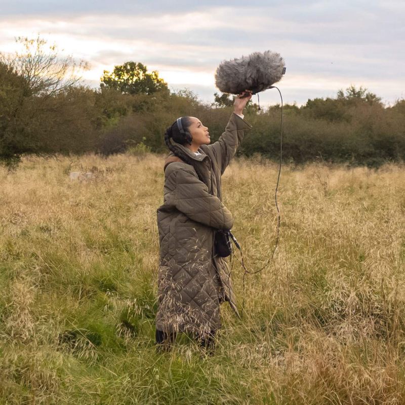 Jayda G hält ein Mikrofon in einer Naturlandschaft hoch.