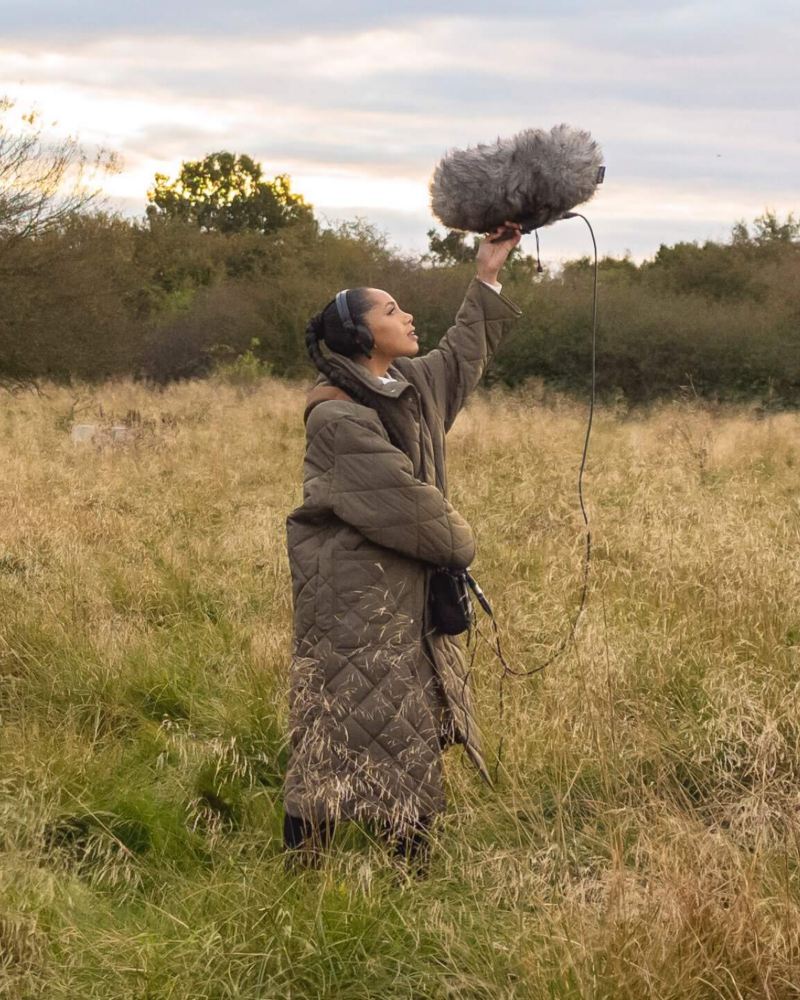 Jayda G solleva un microfono in un paesaggio naturale.