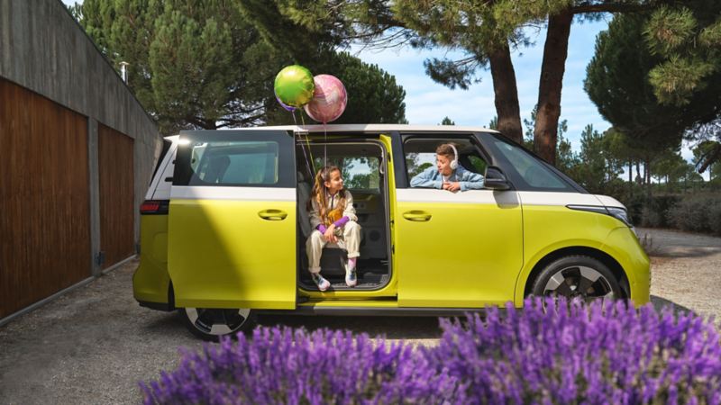 En gulvit VW ID Buzz elbil från sidan med en liten flicka som sitter i den öppna skjutdörren