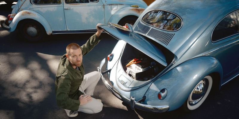 Ewan McGregor kniet vor blauem Käfer mit geöffneter Motorhaube 