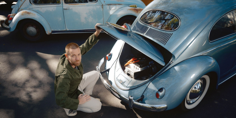 Ewan McGregor s’inginocchia davanti a un Maggiolino blu con il cofano motore aperto