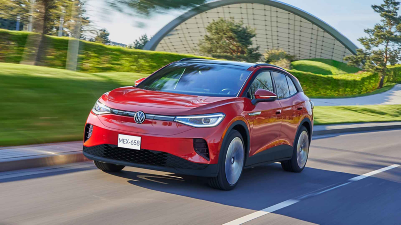 ID.4 de Volkswagen circula por una calle con áreas verdes y un edificio moderno al fondo. 