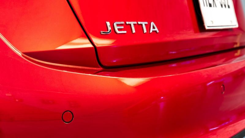 Pareja recargada en la puerta de conductor de Volkswagen Jetta 2024, color rojo.