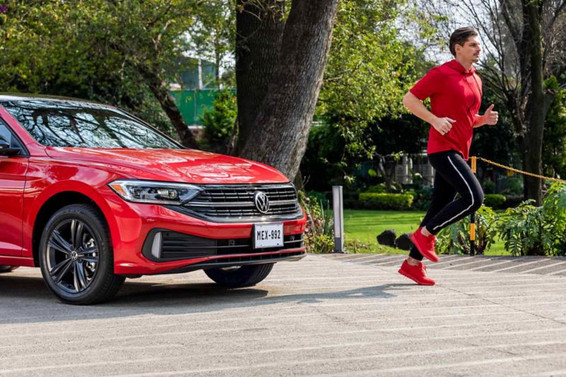 Jetta 2022 en color rojo con hombre que corre delante de auto sedán mexicano. 