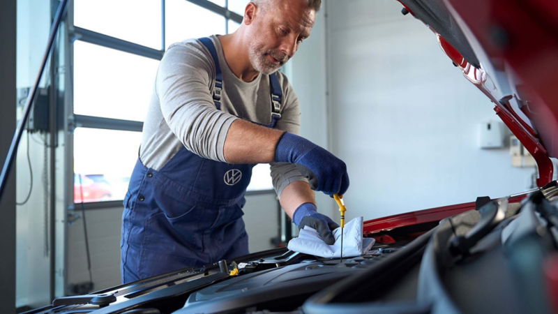 Técnico de Volkswagen revisa el nivel de aceite de motor en auto VW. 