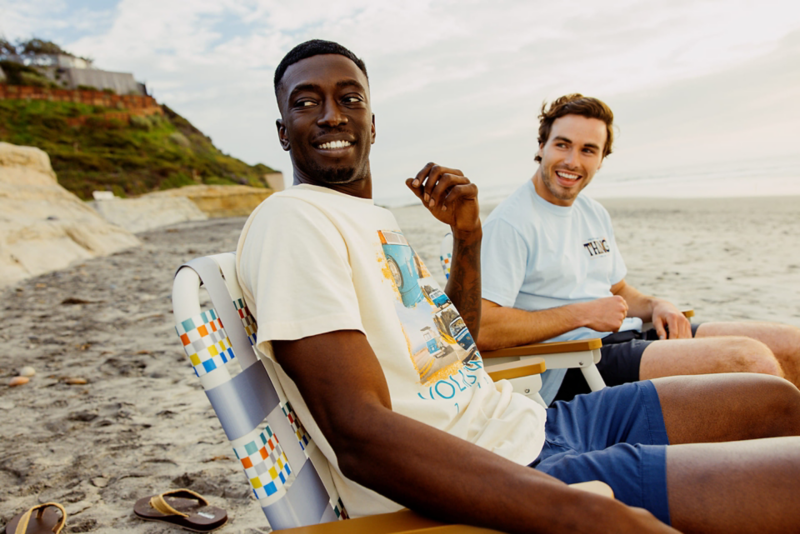 Dos amigos se relajan en una playa, charlando en coloridas sillas junto al mar.