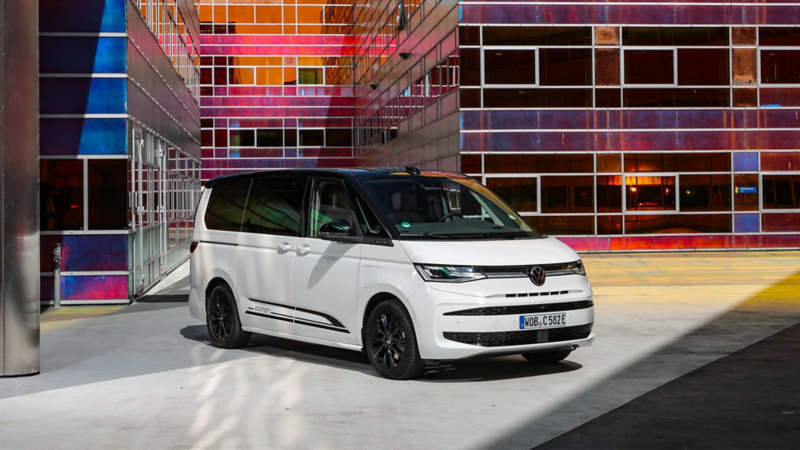 Nya VW Multivan eHybrid framför en färggrann byggnad.