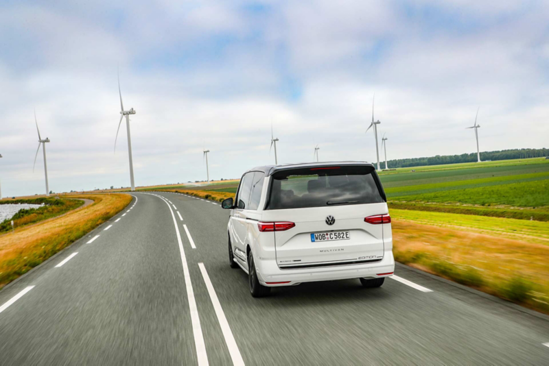 VW Multivan eHybrid bakifrån kör mot en vindkraftspark.