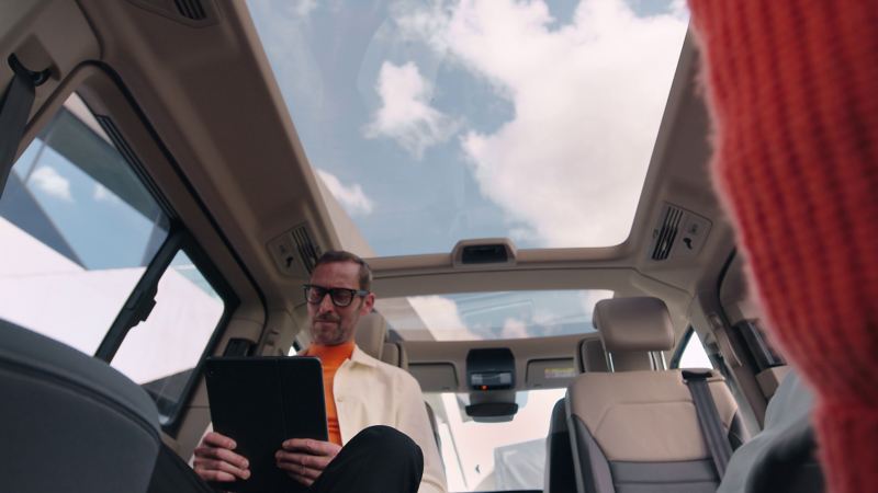 En man sitter och arbetar i en VW Multivan T7 med panoramaglastaket i bakgrunden