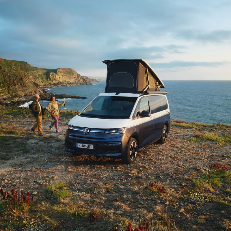 Zwei nebeneinanderstehende VW California mit aufgestelltem Hochstelldach und geöffneten Schiebetüren.