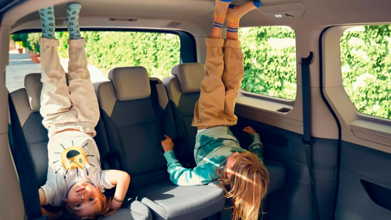 Deux enfants se tiennent la tête en bas sur la banquette arrière d’un VW Multivan et jouent joyeusement dans l’habitacle lumineux.