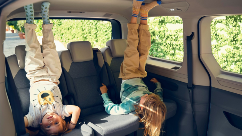Deux enfants se tiennent la tête en bas sur la banquette arrière d’un VW Multivan et jouent joyeusement dans l’habitacle lumineux.