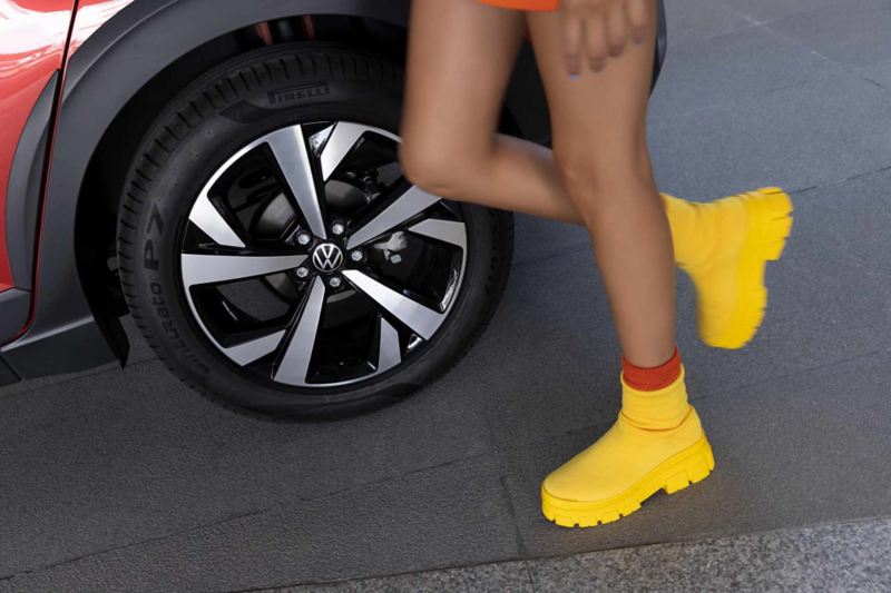 Mujer con botas amarillas camina cerca de llanta de Nivus VW, versión Highline.