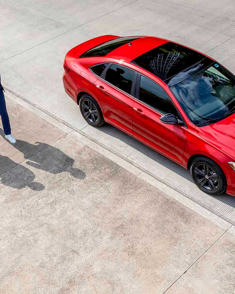 Nuevo Jetta 2022 - Auto sedán mexicano de color rojo. Pareja camina a lado de vehículo Volkswagen. 