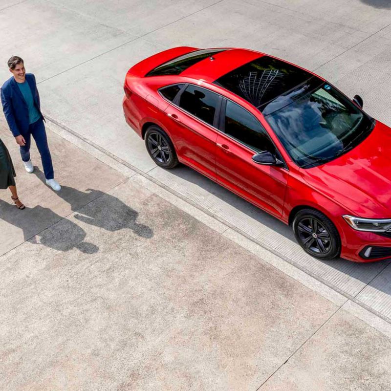 Nuevo Jetta 2022 - Auto sedán mexicano de color rojo. Pareja camina a lado de vehículo Volkswagen. 