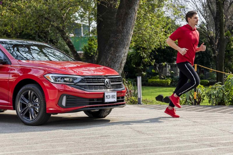 Jetta 2022 en color rojo con hombre que corre delante de auto sedán mexicano. 