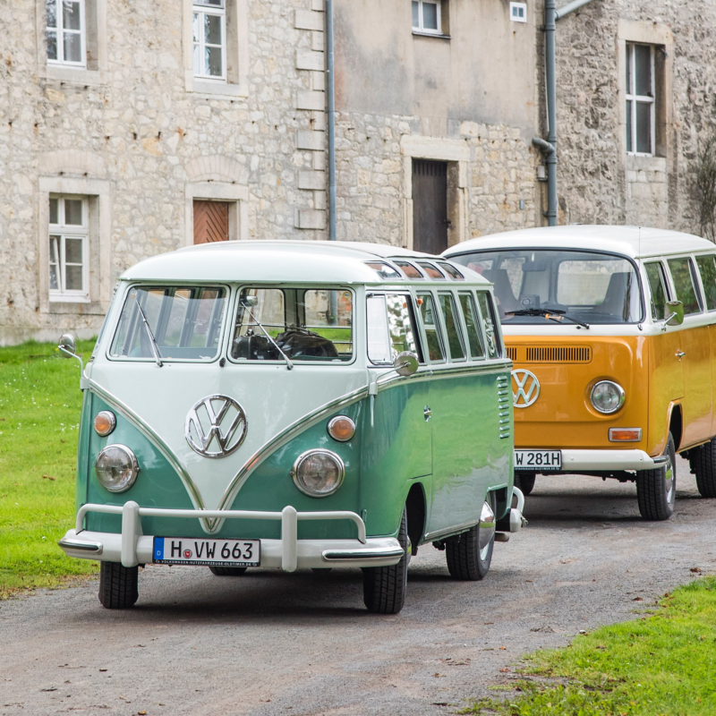 Zwei ältere VW Busse fahren eine Straße entlang.