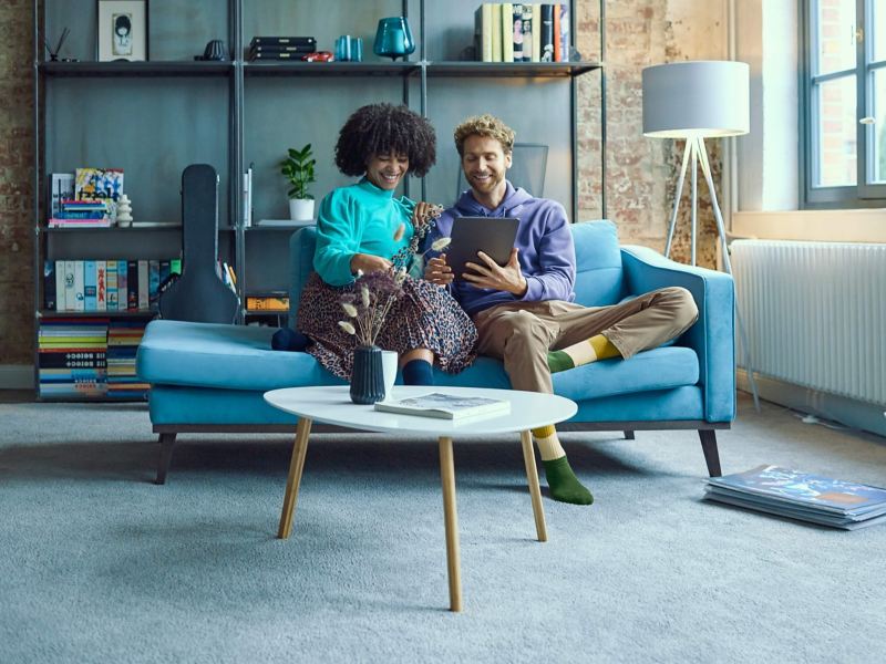 Ein Mann und eine Frau sitzen auf einer Couch und gucken einen Laptop Bildschirm an.
