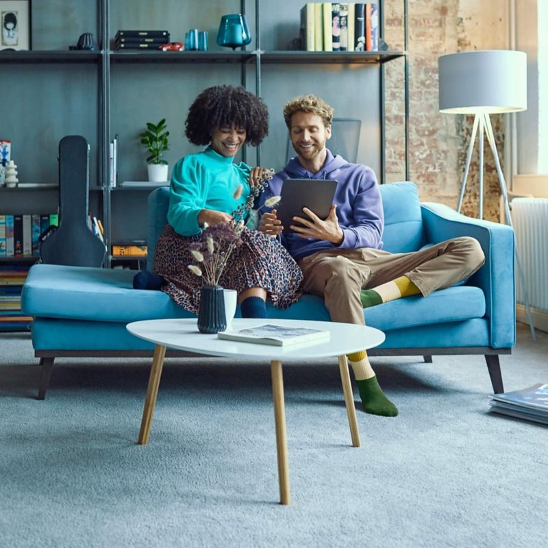 Ein Mann und eine Frau sitzen auf einer Couch und gucken einen Laptop Bildschirm an.
