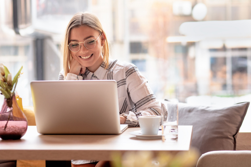 Eine junge Frau sitzt lächelnd vor ihrem Laptop am Schreibtisch