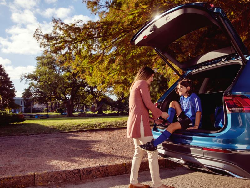 A young girl sitting in the trunk of VW SUV while her mom helps to tie a shoe, outgoing link to volkswagenplus.ca/en
