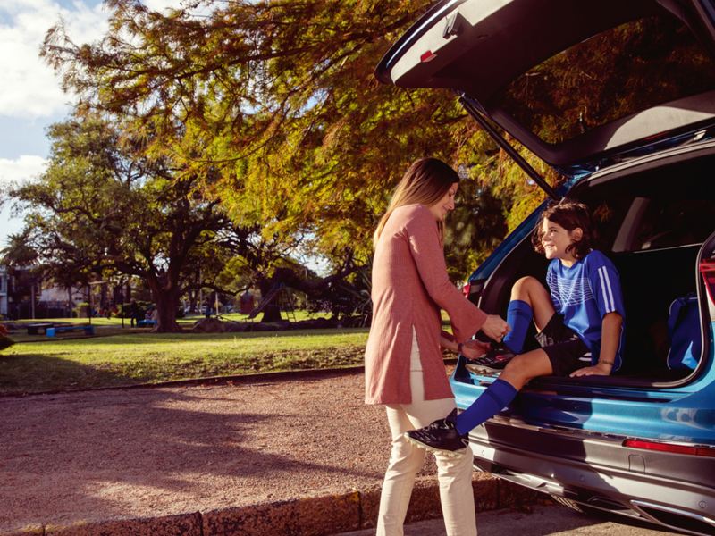 A young girl sitting in the trunk of VW SUV while her mom helps to tie a shoe, outgoing link to volkswagenplus.ca/en