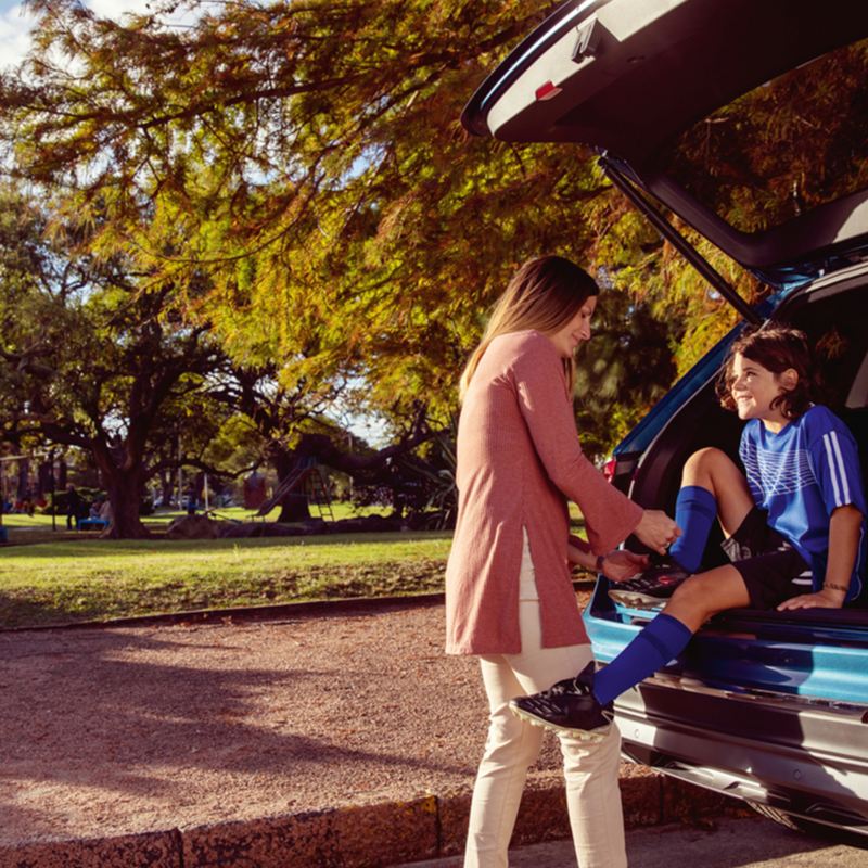 A young girl sitting in the trunk of VW SUV while her mom helps to tie a shoe, outgoing link to volkswagenplus.ca/en