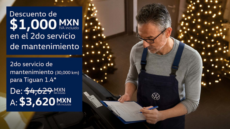 Técnico de Volkswagen revisa hoja de servicio frente a motor de auto con luces navideñas al fondo.