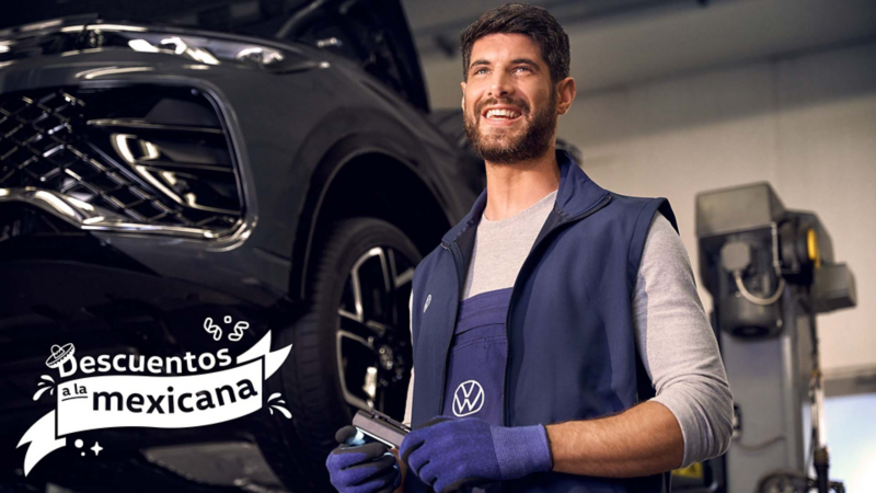 Técnico VW sonriente en el taller, con un coche levantado en segundo plano.