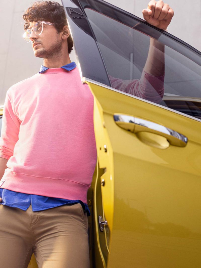 Hombre con suéter rosa posa sobre Nuevo T Cross de Volkswagen, mientras sujeta puerta de copiloto.