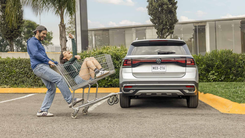 Pareja juega con un carrito de super a lado de una camioneta SUV Taigun 2025.