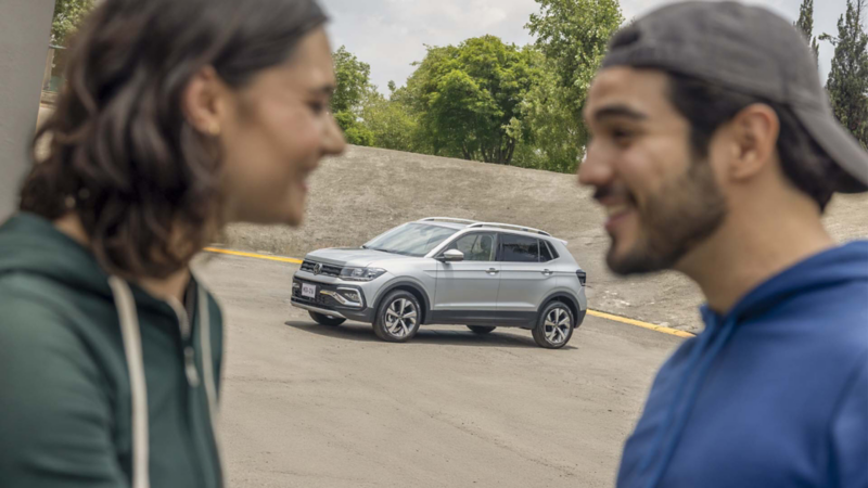 SUVW compacta Taigun 2025 de color gris en segundo plano con pareja desenfocada.