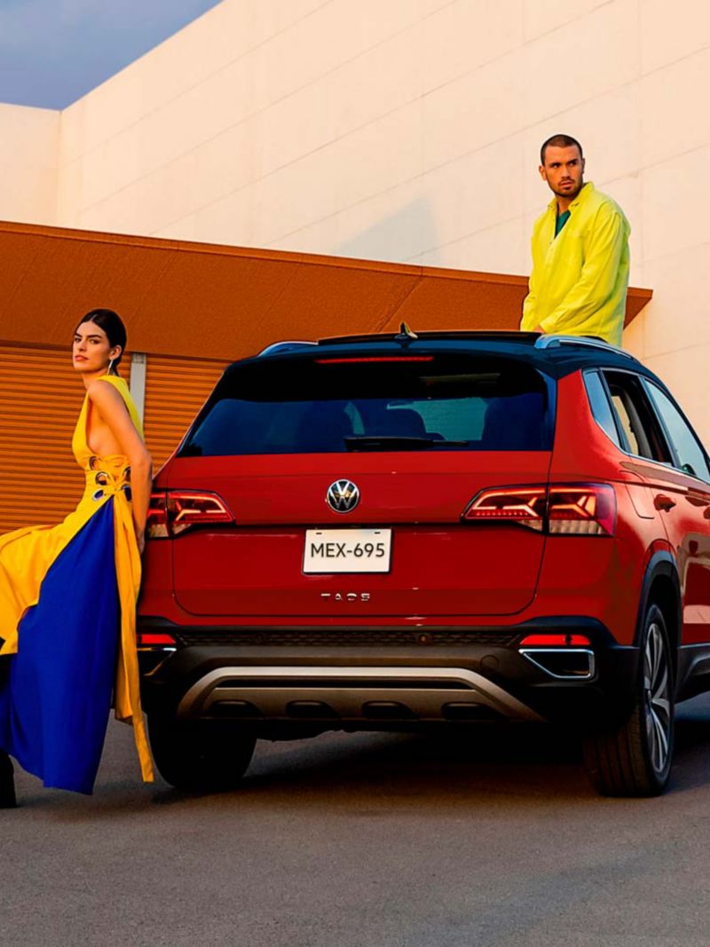 Taos 2024, camioneta Volkswagen para cinco pasajeros en color rojo, con pareja recargada en SUV.