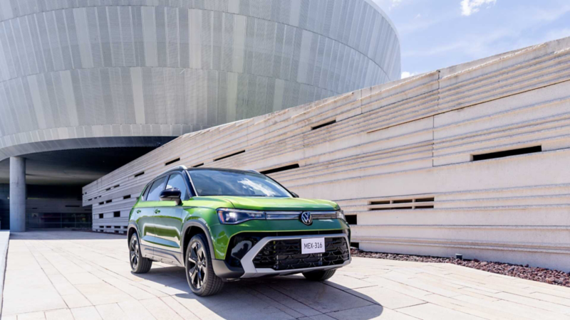 VW Taos verde frente a un edificio moderno de formas curvas y muros de piedra.