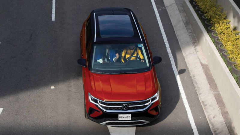 Taos 2024, camioneta Volkswagen para cinco pasajeros en color rojo, con pareja recargada en SUV.