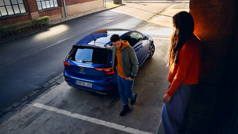A man standing next to a blue VW Polo with his hand on the roof, with a woman standing nearby