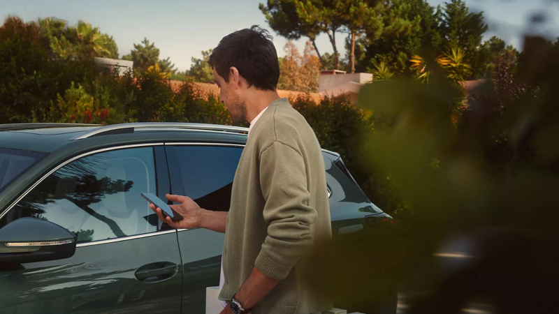 A man standing next to a green VW, looking at the smartphone in his hand