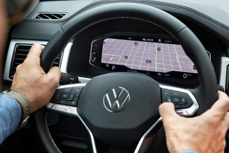 Manos agarran un volante multifunciones. Al fondo, la pantalla del Volkswagen Digital Cockpit en Teramont 2022.