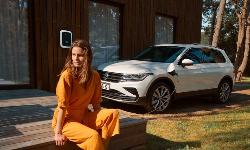 Woman sitting in front of a VW Tiguan charging at a wallbox.