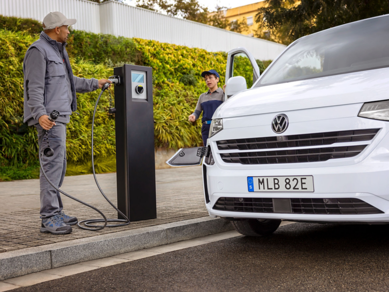 En man står vid en laddstolpe och laddar sin VW e-Transporter