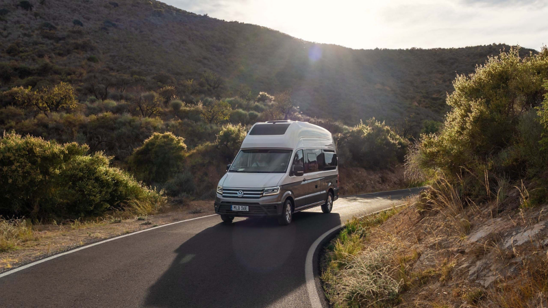 VW Grand California husbil kör på en landsväg bland bergen