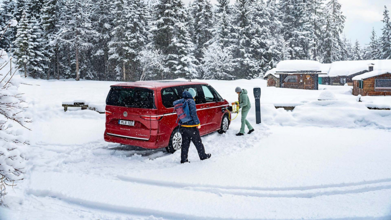 En Multivan eHybrid står parkerad vid ett hus med en elbilsladdare