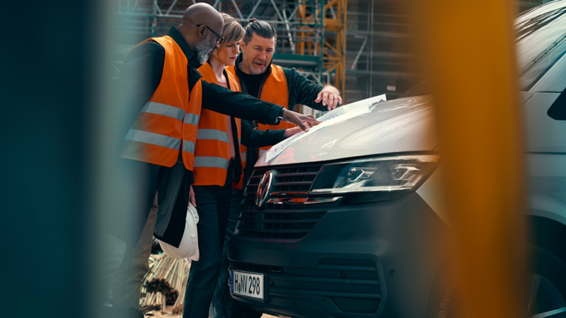 Två män och en kvinna diskuterar en ritning vid en VW Transporter Skåp