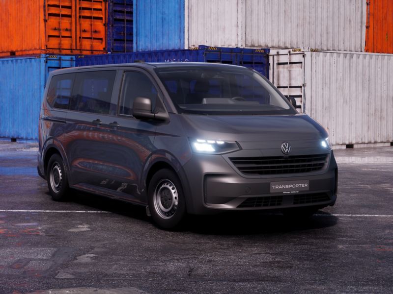 Photo of a black New Transporter parked in front of towers of sea containers. 