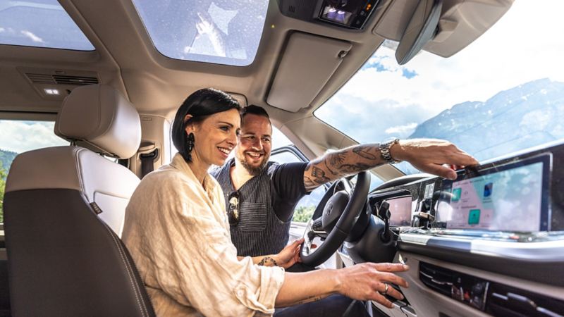Marc und Brigitte Trauffer betrachten gemeinsam das Infotainment-System des neuen VW Multivan eHybrid.