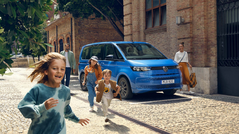 Glada barn framför en blå VW Multivan eHybrid minibuss